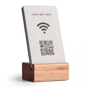Könnte beinhalten: Eine rechteckige weiße Karte mit dem Text "YOUR WIFI TEXT", einem WLAN-Symbol und einem QR-Code, die auf einem Holzständer angezeigt wird. Der Ständer besteht aus hellbraunem Holz. Die Karte ist leicht nach hinten geneigt.