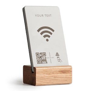 Könnte beinhalten: Eine rechteckige silberne Karte mit dem Text "YOUR TEXT" und einem Wi-Fi-Symbol, QR-Code und NFC-Symbol, die auf einem Holzständer präsentiert wird. Der Ständer ist aus hellem Holz gefertigt.