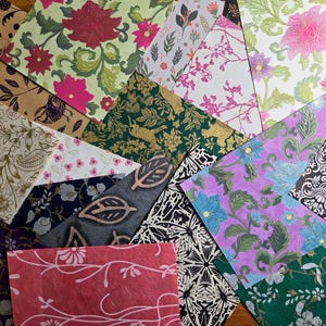 May include: A collection of rectangular paper sheets featuring diverse patterns including floral, botanical, paisley, and geometric designs in colors such as red, green, purple, black, white, and gold, arranged in an overlapping, layered composition.