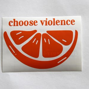 Puede incluir: Pegatina naranja con el texto "choose violence" y un gr&aacute;fico estilizado de rodaja de naranja.