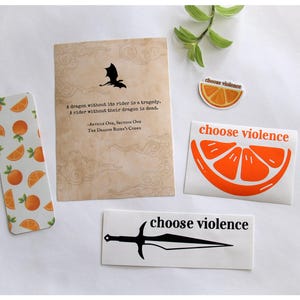 May include: A collection of stickers and a bookmark with orange and dragon-themed designs. The bookmark features oranges, while the stickers display an orange slice and the phrase "choose violence" with a sword graphic. A card with a dragon silhouette and quote is also present.