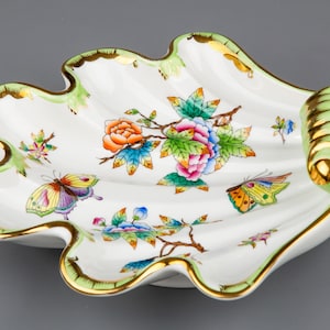 May include: A white porcelain serving dish shaped like a seashell with a green and gold rim. The dish is decorated with a floral pattern and butterflies.