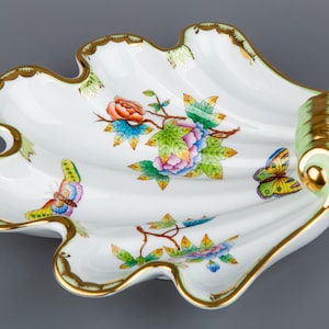 May include: A white porcelain shell-shaped dish with a green handle and gold trim. The dish is decorated with colorful flowers, butterflies, and green leaves.
