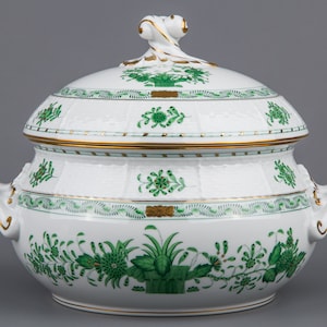 May include: A white porcelain tureen with a lid, featuring a green and gold floral pattern. The tureen has two handles and a decorative knob on the lid.