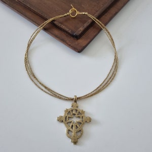 Könnte beinhalten: Eine goldene Halskette mit einer mehrlagigen Kette und einem großen, verzierten Kreuzanhänger.