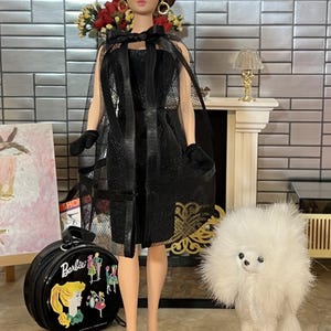May include: A vintage Barbie doll in a black dress and cape, with a matching handbag and a white toy poodle. The doll is posed on a black stand. The background includes a fireplace and a painting. The doll's accessories include black gloves.