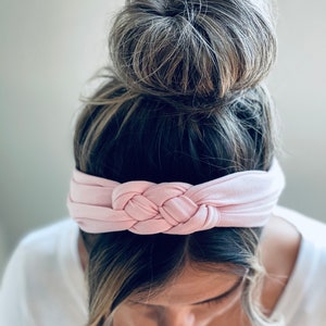 Op de afbeelding: Een lichtroze geknoopt hoofdband voor vrouwenhaar. Het hoofdband is gemaakt van een zachte, rekbare stof en is ontworpen om comfortabel te dragen.