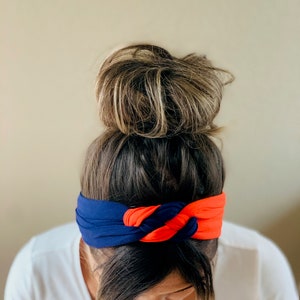 May include: A woman with brown hair in a bun is wearing a blue and orange knotted headband.