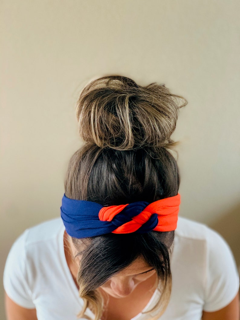 May include: A woman with brown hair in a bun is wearing a blue and orange knotted headband.