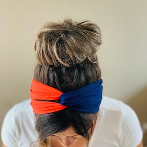 May include: A woman wearing a blue and orange headband. The headband is twisted and knotted. The woman has her hair pulled back in a bun.