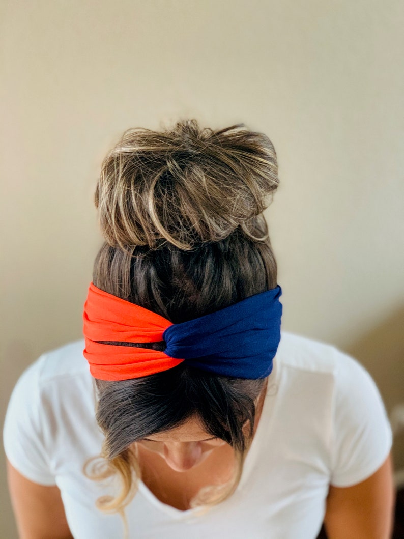 May include: A woman wearing a blue and orange headband. The headband is twisted and knotted. The woman has her hair pulled back in a bun.