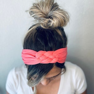 Op de afbeelding: Een roze geknoopt hoofdband van zachte stof. Het hoofdband wordt gedragen door een persoon met blond haar in een knot.