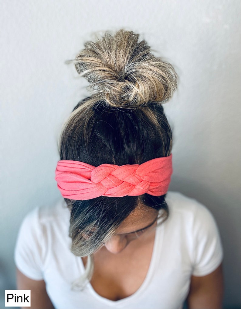 Op de afbeelding: Een roze geknoopt hoofdband van zachte stof. Het hoofdband wordt gedragen door een persoon met blond haar in een knot.