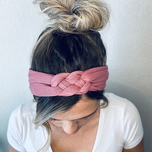 Op de afbeelding: Een mauve geknoopt hoofdband gemaakt van zachte stof. Het hoofdband wordt gedragen door een persoon met blond haar dat in een knot is getrokken.
