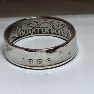 Könnte beinhalten: Ein silberner Ring aus einer 25-Cent-Münze von 1985. Der Ring ist mit "Quarter Dollar" und dem Jahr "1985" graviert.