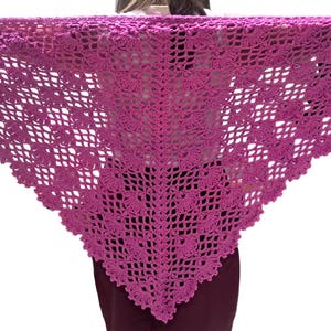 May include: A magenta crochet shawl with a triangular shape. The shawl features an openwork design with floral and geometric patterns. The edges are scalloped, adding a decorative touch. The shawl is made of a soft, lightweight yarn, perfect for layering.