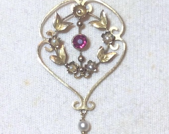 May include: A gold-toned pendant necklace featuring an open, heart-shaped frame. The center contains a circular magenta gemstone surrounded by small white floral accents and gold leaves. A single white pearl hangs from the bottom of the frame.