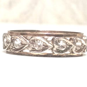 May include: A silver band ring with a row of small diamonds set in heart-shaped designs.