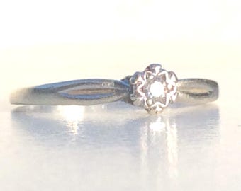 Puede incluir: Un delicado anillo de plata con un pequeño diamante engastado en un diseño con forma de flor.