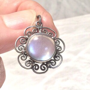 May include: A circular pendant featuring a central iridescent cabochon stone set in a silver-toned metal frame. The frame is decorated with intricate wire scrollwork and small spherical accents, forming a flower-like shape with a top bail.