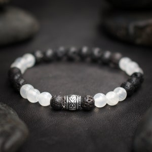 Könnte beinhalten: Ein schwarz-weißes Perlenarmband mit einem silbernen Anhänger. Das Armband besteht aus Lava- und weißen Mondsteinperlen.