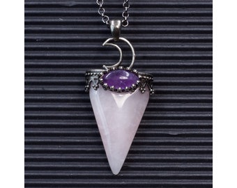 Puede incluir: Un colgante de plata con una punta de cuarzo rosa y una piedra de amatista púrpura. El colgante tiene forma de lágrima y tiene un dije de luna creciente en la parte superior.