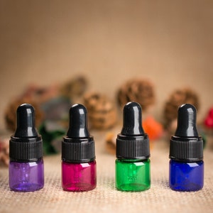 May include: Four small glass bottles with black dropper tops. The bottles are filled with different colored liquids: purple, pink, green, and blue.