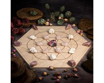 May include: A wooden hexagonal crystal grid with a geometric design. The grid is surrounded by various crystals, including pink, white, and grey stones. The grid is set on a dark grey surface with dried flowers and leaves.