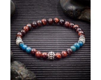 Puede incluir: Un brazalete de cuentas con piedras rojas, azules y blancas. El brazalete tiene una cuenta de plata en el centro.