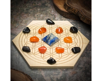 May include: A hexagonal wooden board with a flower of life design, surrounded by orange and black polished stones. A blue and white pyramid-shaped stone sits in the center. The board is made of light-colored wood.