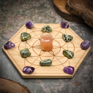 Könnte beinhalten: Ein sechseckiges Kristallgitter aus Holz mit einem geometrischen Muster, in dessen Mitte sich ein hellorangener Kristall befindet, der von acht Kristallen umgeben ist: sechs violetten Amethystkristallen und zwei grünen Kristallen.