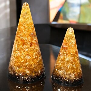 May include: Two cone-shaped decorative objects. The objects are filled with gold and amber-colored materials, with a dark base. The larger cone is approximately 6 inches tall, and the smaller one is about 4 inches tall.