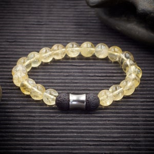 Könnte beinhalten: Ein Armband aus gelbem Citrin mit schwarzen Lavasteinen und einem silbernen Metallakzent.