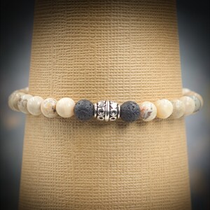 May include: A beaded bracelet with white and brown stones and a black lava bead with a silver spacer bead.