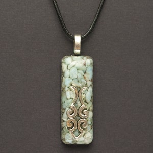 May include: A silver pendant necklace with a rectangular charm filled with light blue and white stones. The charm has a silver design in the center.