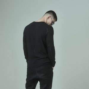 May include: A man wearing a black long-sleeved shirt and black shorts. He is wearing black boots with zippers on the back.