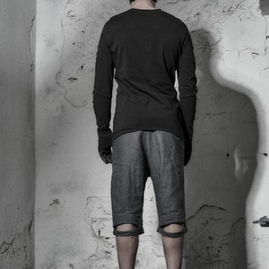 May include: A person wearing a black long-sleeved shirt, black shorts with knee pads, and black shoes. The person is standing in a room with a white wall.