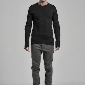 May include: A man wearing a black long-sleeved shirt with a black beanie and mirrored sunglasses. He is wearing gray pants and black shoes.
