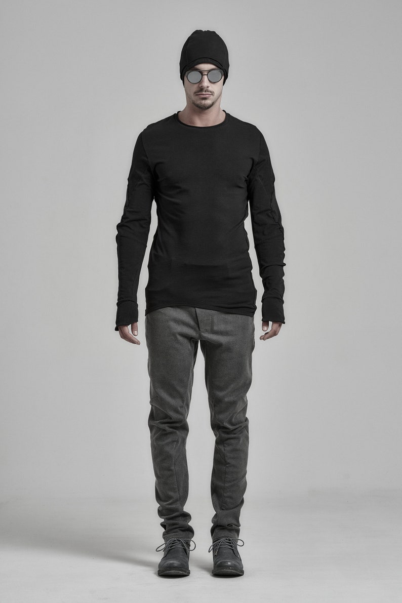 May include: A man wearing a black long-sleeved shirt with a black beanie and mirrored sunglasses. He is wearing gray pants and black shoes.
