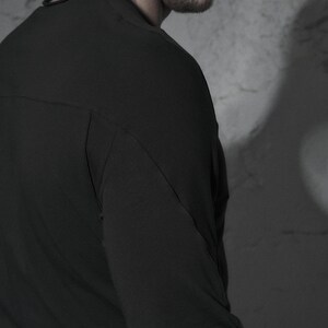 May include: A black long-sleeved shirt with a slightly fitted silhouette. The shirt has a simple design and a smooth texture.