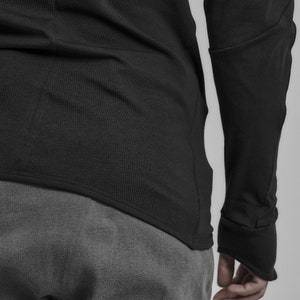May include: A black long-sleeved shirt with a curved hemline and a grey pair of pants.