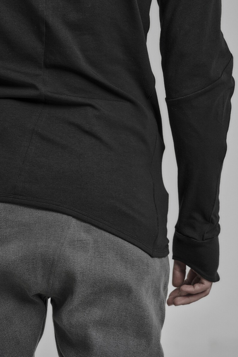 May include: A black long-sleeved shirt with a curved hemline and a grey pair of pants.