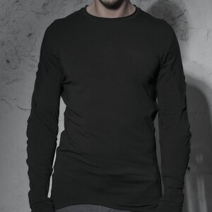 May include: A black long-sleeved shirt with a round neckline and black fingerless gloves. The person is wearing a black beanie and sunglasses.