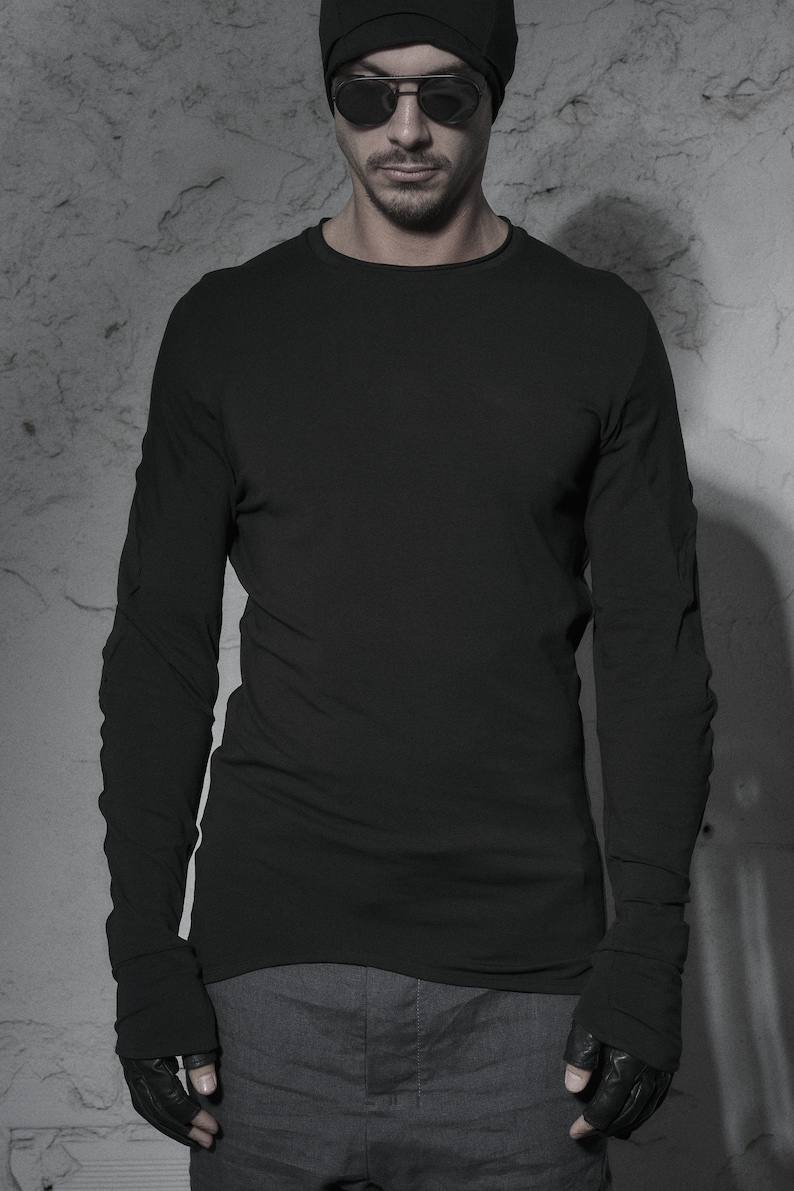 May include: A black long-sleeved shirt with a round neckline and black fingerless gloves. The person is wearing a black beanie and sunglasses.