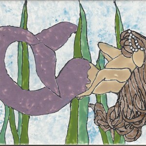May include: A purple mermaid with long brown hair is swimming in a bed of green seaweed. The mermaid is wearing a pearl crown.