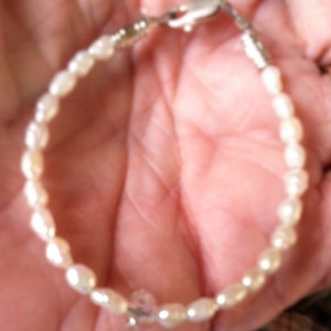 May include: A white pearl bracelet with a silver clasp and a clear crystal charm.