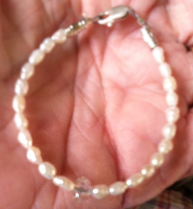 May include: A white pearl bracelet with a silver clasp and a clear crystal charm.