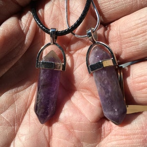May include: Two amethyst crystal point pendants on black and silver chains. The pendants are in the shape of a point with a silver setting.