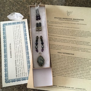 May include: A silver necklace with a green, grey, and black stone pendant. The necklace is made of various beads, including amethyst, hematite, and clear quartz. The necklace is in a small box with a white background. The text on the card reads "Intuition, Inspiration, Imagination (Charged at the Borton Canyon Vortex)".