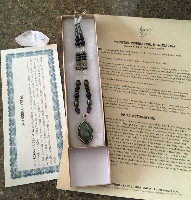 May include: A silver necklace with a green, grey, and black stone pendant. The necklace is made of various beads, including amethyst, hematite, and clear quartz. The necklace is in a small box with a white background. The text on the card reads "Intuition, Inspiration, Imagination (Charged at the Borton Canyon Vortex)".